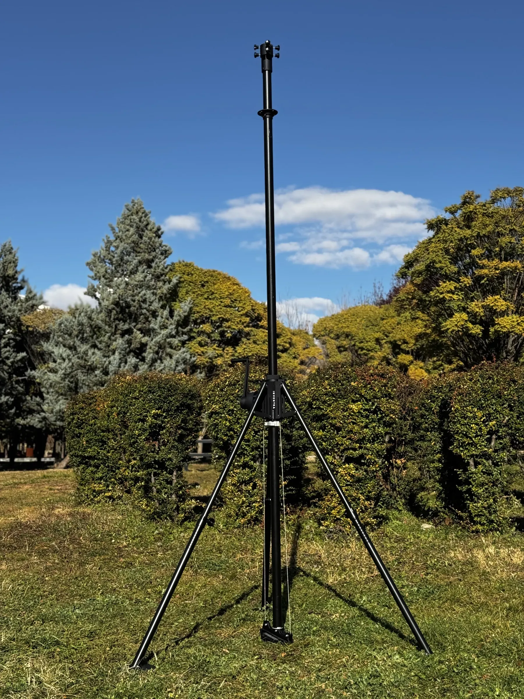 Portatif tripod mast çimende tam açılmış; mavi gökyüzü ve sonbahar ağaçları