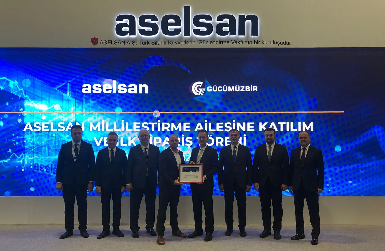 ASELSAN’ın millîleştirme programına katılım ve ilk sipariş töreninde sekiz kişi; biri çerçeveli belgeyi tutuyor