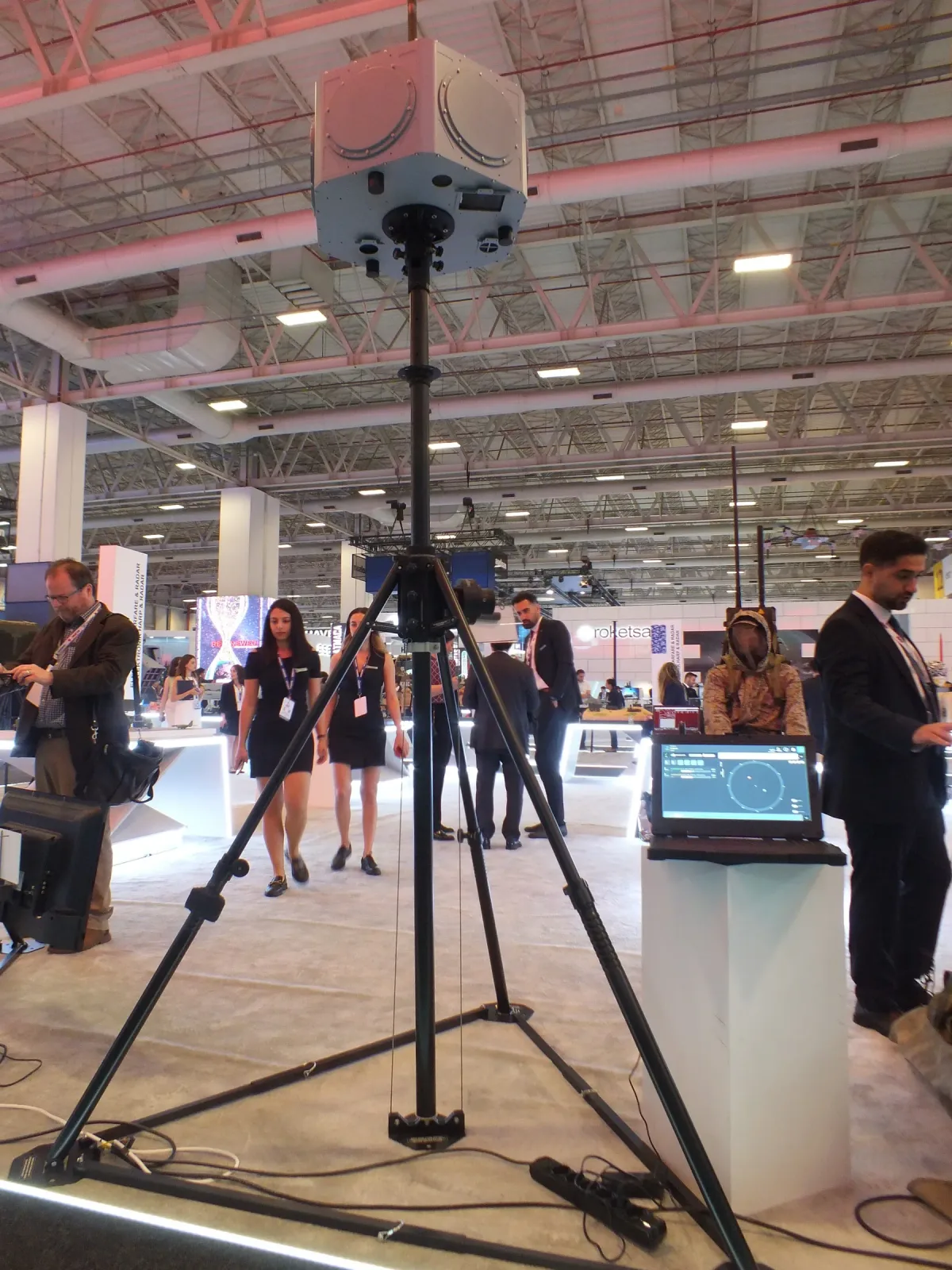 Fuar zemininde kurulmuş portatif tripod-mast; gergi halkaları ve faydalı yük başı görünüyor