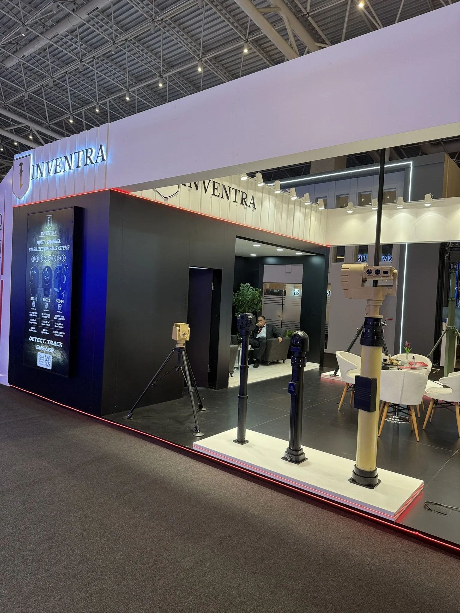 Standın yanı; beyaz platform boyunca üçayaklar ve mastlar, uç duvarda gimbal afişi