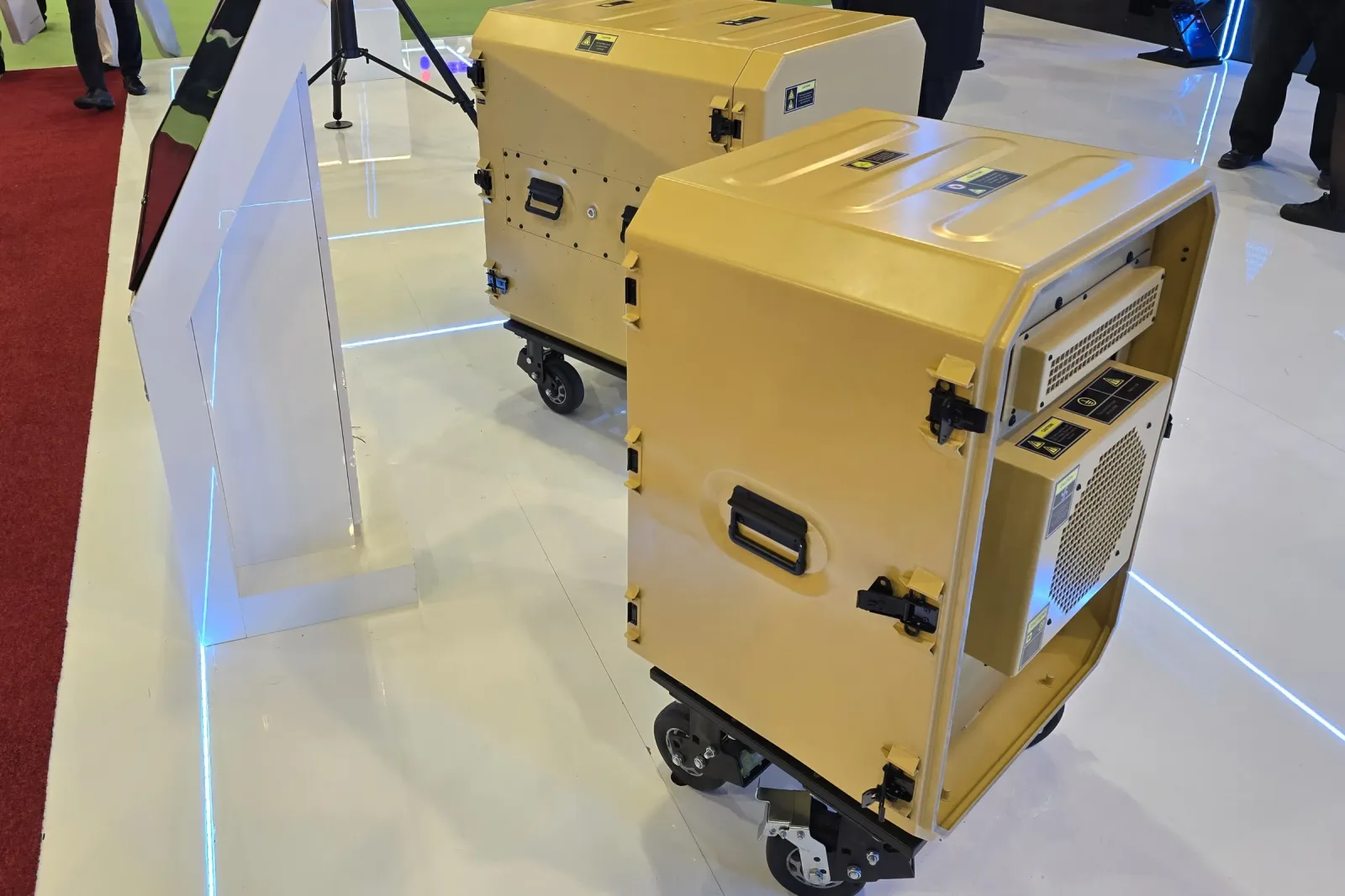 Stand koridorundan çekilmiş iki rack kabin; önde salonun kırmızı halısı