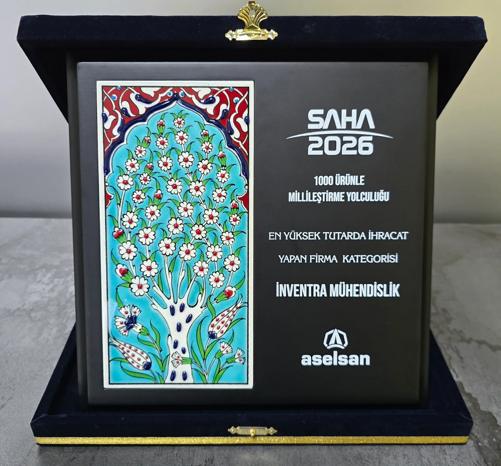 Açık kutusunda plaket: solda el boyaması İznik çini paneli, sağda kazınmış metin — SAHA 2026, millileştirme programının adı, ödül kategorisi ve İnventra Mühendislik; altta ASELSAN logosu