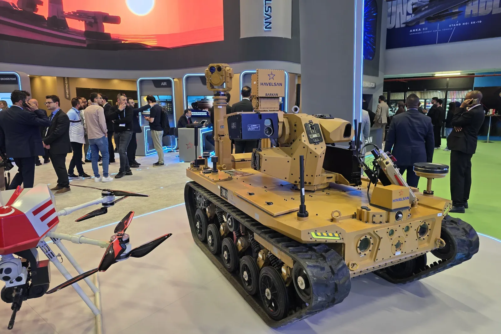 Kapalı alandaki standda paletli insansız kara aracı; gövdesinin üzerinde mast üstü stabilize gimbal taşıyor