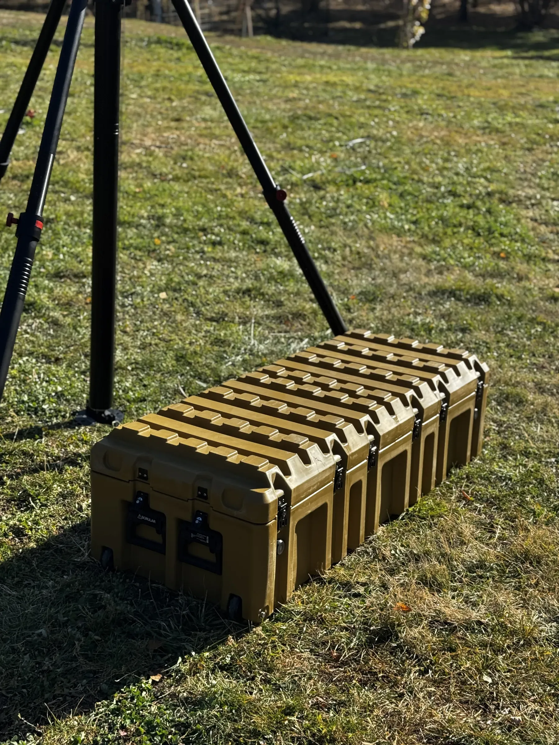 Çimene sabitlenmiş tripod ayakları ve yanında sistemin kapalı zeytin yeşili sağlamlaştırılmış taşıma sandığı