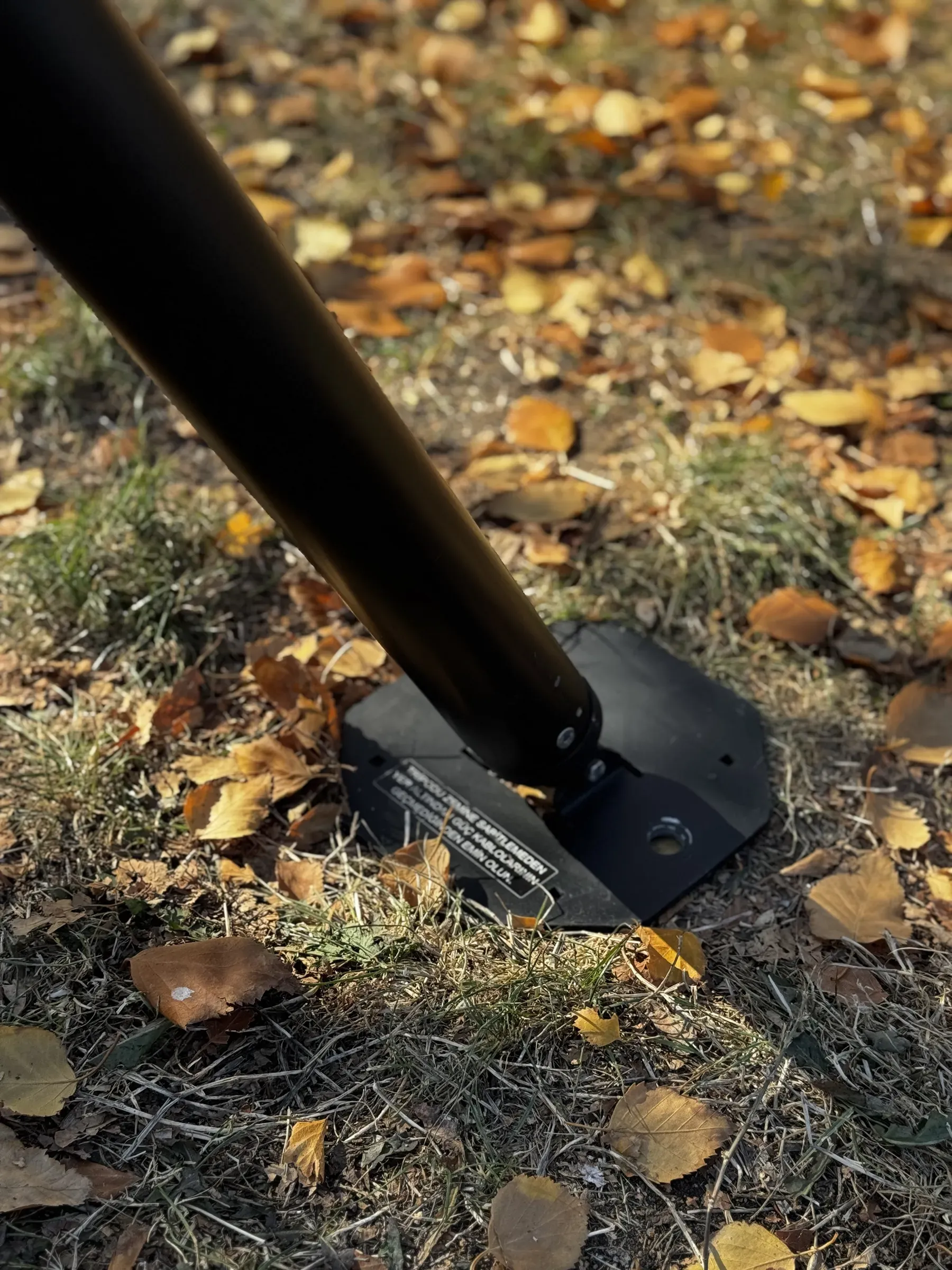 Yaprak kaplı zeminde ayak plakasına basan bir tripod ayağının yakın mesafeden çekimi