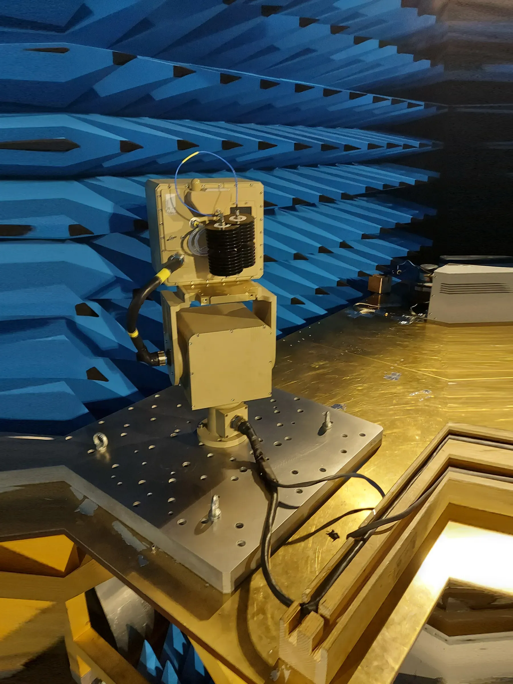 Mavi absorban kaplı odada tezgâhtaki metal test fikstürüne cıvatalanmış çöl rengi pozisyoner