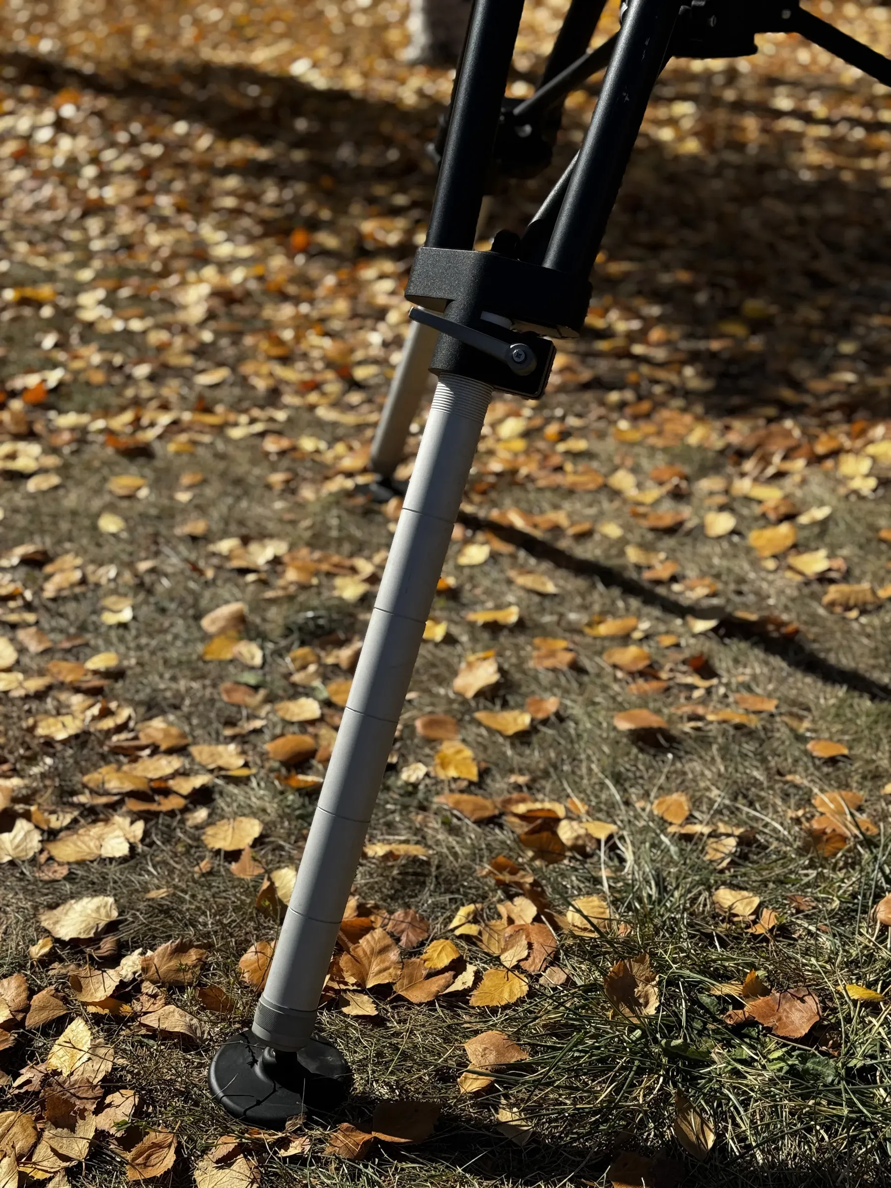 Dökülmüş yaprakların üzerinde kelepçesi ve lastik ayağıyla bir TMH10 tripod ayağının yakın görünümü